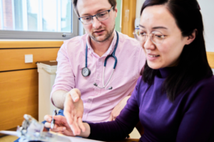 Image of a GP talking to a person with a clipboard. The GP is pointing towards the clipboard.