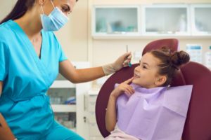 Image of a dentist treating a child. The child is sat in the dentist chair. She is smiling