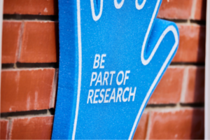 Close up image of foam hand against a brick wall with text that reads: Be part of research