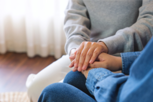 Image of a person sat next to another person. One person is holding the other person's hand.